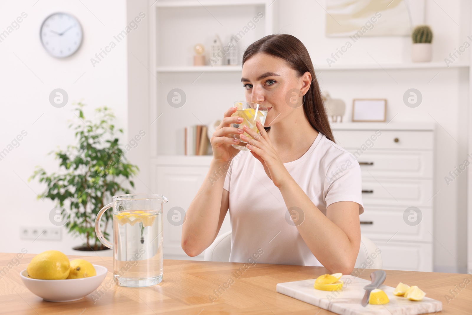 Photo of Woman drinking water with lemon at table indoors