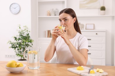 Photo of Woman drinking water with lemon at table indoors