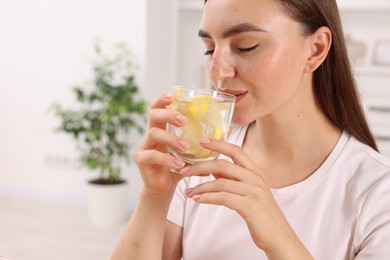 Photo of Woman drinking water with lemon indoors, closeup. Space for text