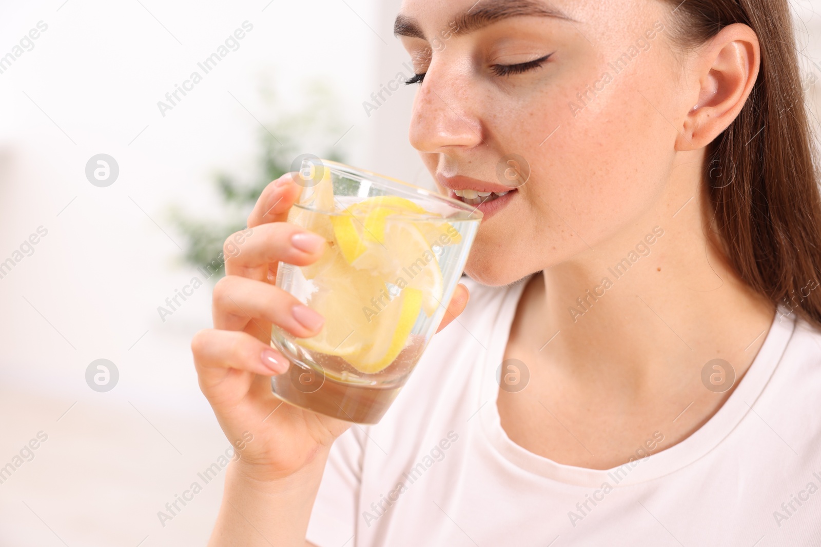 Photo of Woman drinking water with lemon indoors, closeup