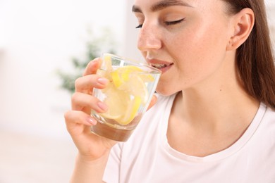 Woman drinking water with lemon indoors, closeup