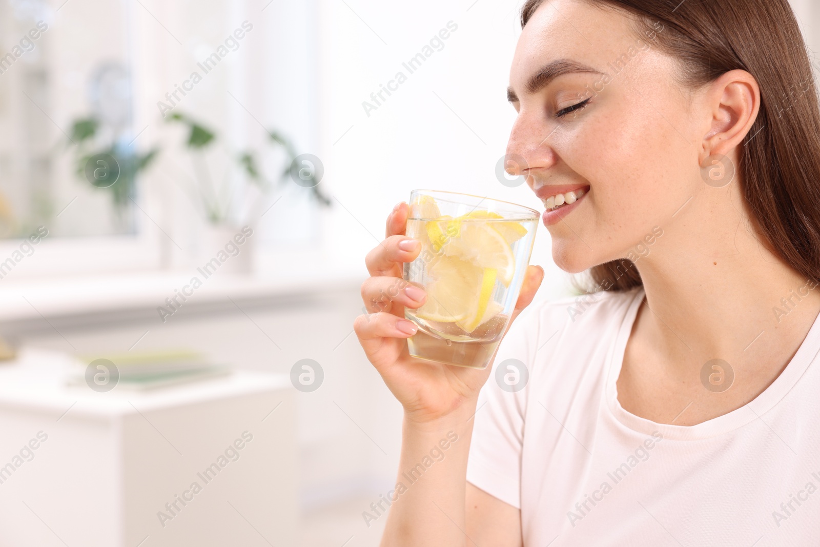 Photo of Woman drinking water with lemon indoors. Space for text