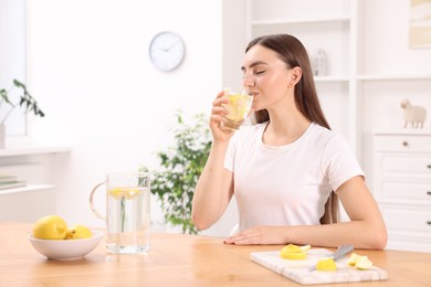 Photo of Woman drinking water with lemon at table indoors