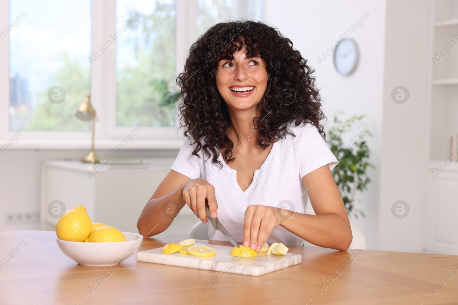 Photo of Making lemon water. Woman cutting fruit at wooden table indoors