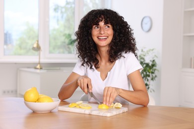 Photo of Making lemon water. Woman cutting fruit at wooden table indoors