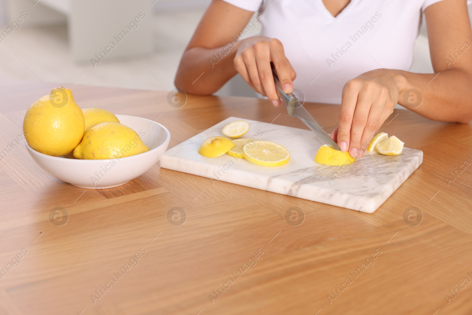 Photo of Making lemon water. Woman cutting fruit at wooden table indoors, closeup