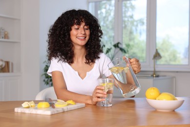 Woman pouring lemon water from jug into glass at table indoors