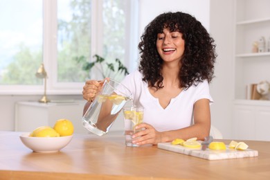 Woman pouring lemon water from jug into glass at table indoors