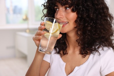 Photo of Beautiful woman drinking water with lemon indoors