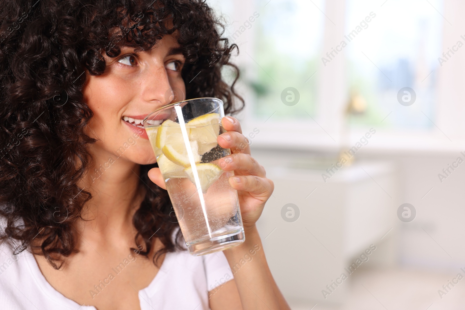 Photo of Beautiful woman drinking water with lemon indoors. Space for text