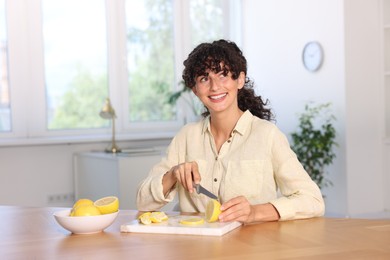 Photo of Making lemon water. Woman cutting fruit at wooden table indoors