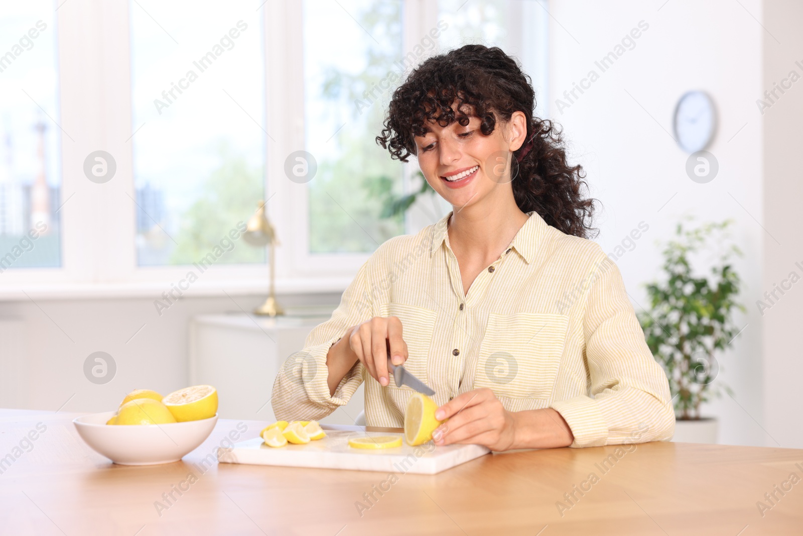 Photo of Making lemon water. Woman cutting fruit at wooden table indoors