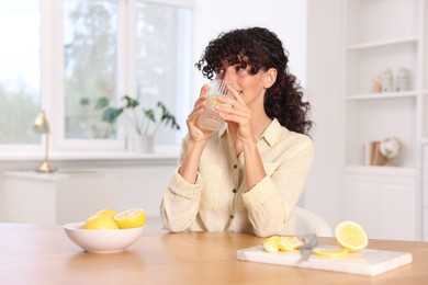 Photo of Woman drinking water with lemon at table indoors