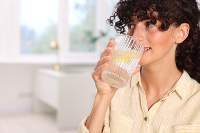 Woman drinking water with lemon indoors. Space for text