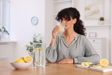 Photo of Woman drinking water with lemon at table indoors