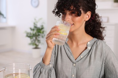 Photo of Beautiful woman drinking water with lemon indoors