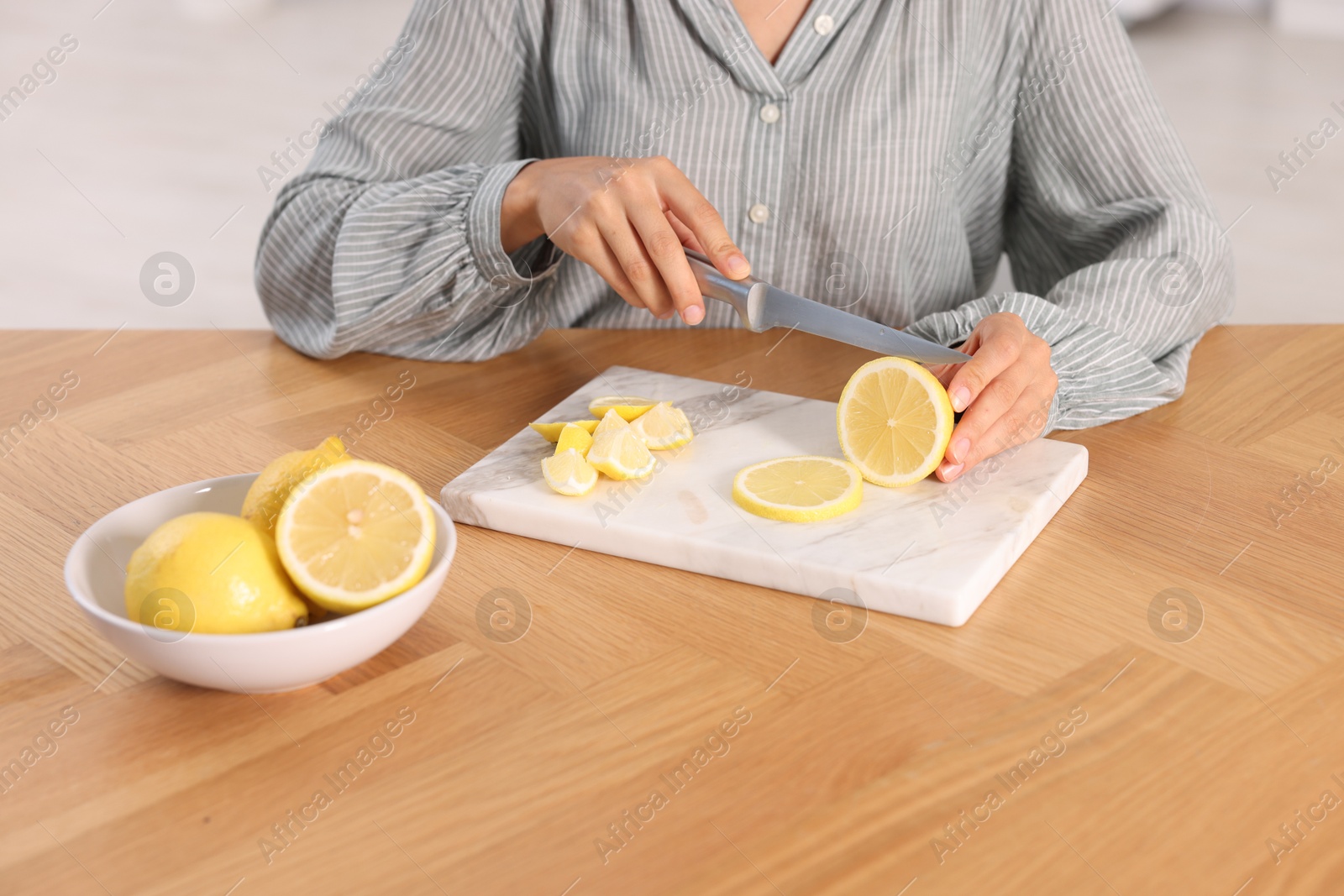 Photo of Making lemon water. Woman cutting fruit at wooden table indoors, closeup