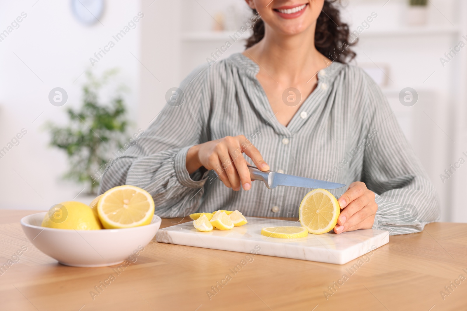 Photo of Making lemon water. Woman cutting fruit at wooden table indoors, closeup