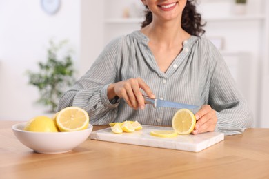 Making lemon water. Woman cutting fruit at wooden table indoors, closeup