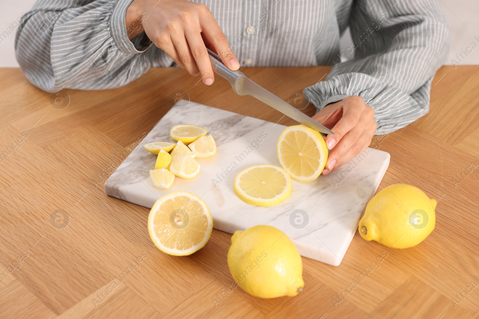 Photo of Making lemon water. Woman cutting fruit at wooden table indoors, closeup