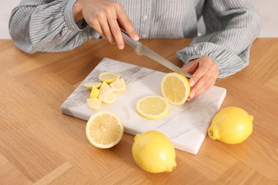 Making lemon water. Woman cutting fruit at wooden table indoors, closeup