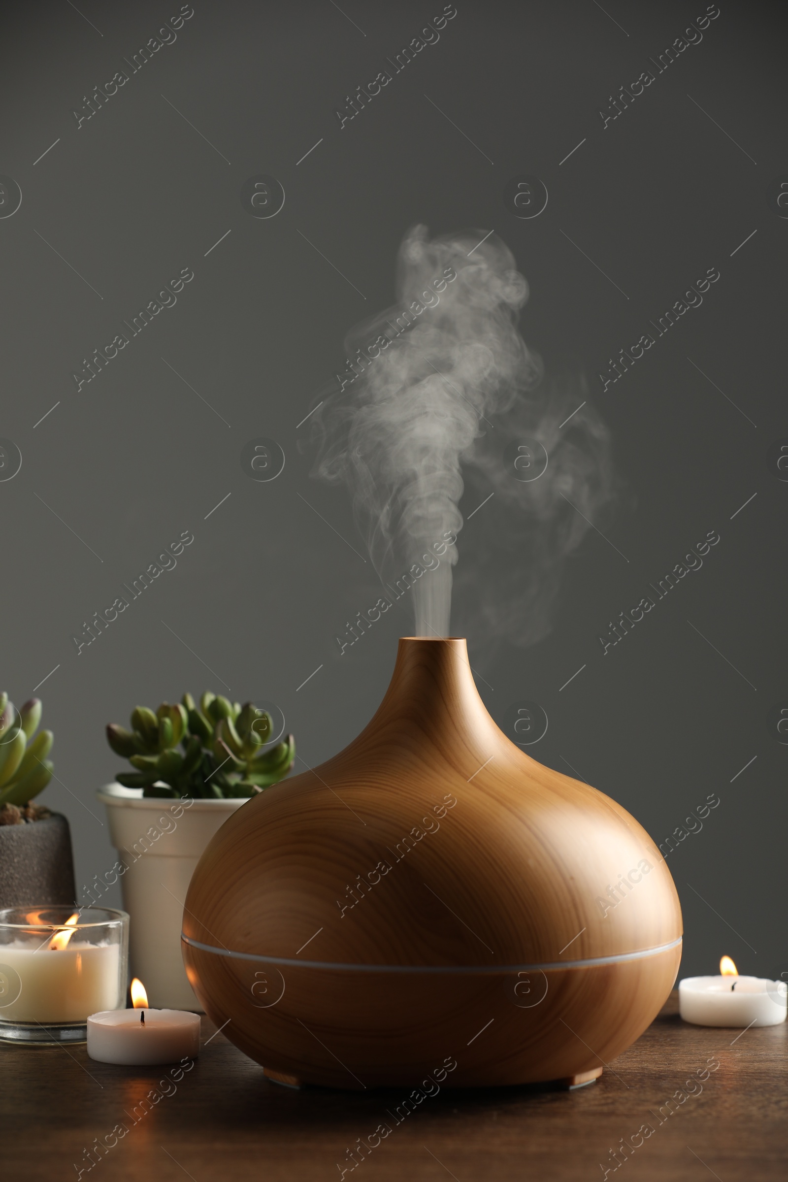 Photo of Aroma oil diffuser, houseplants and burning candles on wooden table