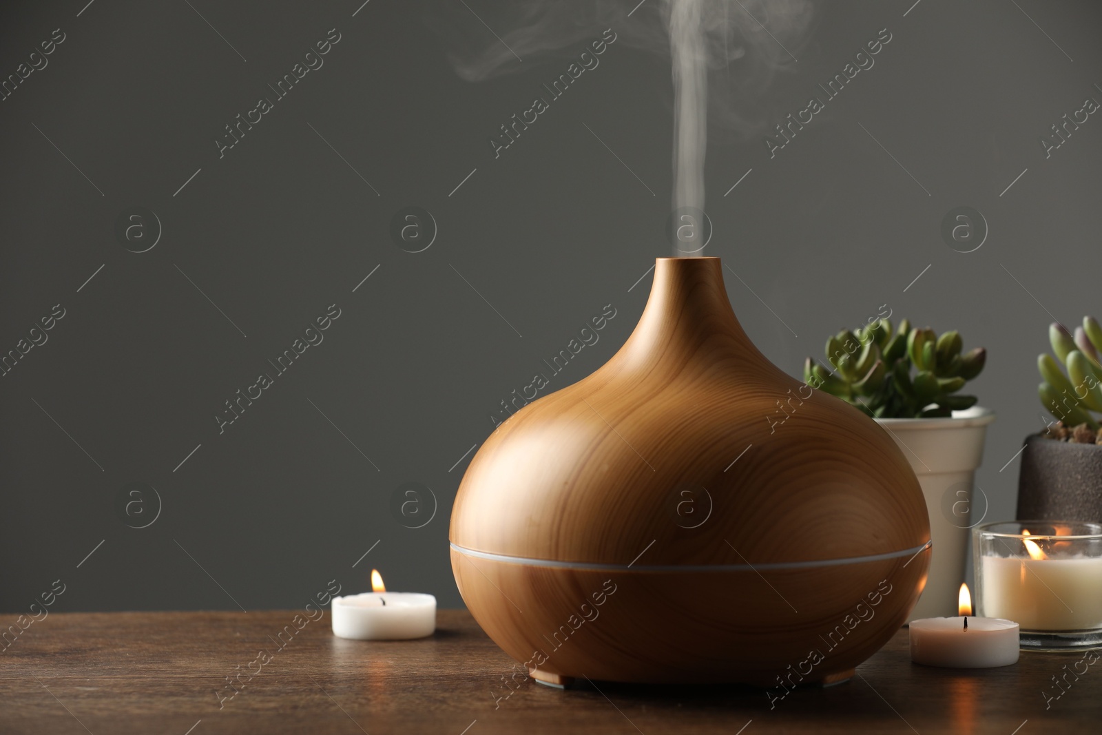 Photo of Aroma oil diffuser, houseplants and burning candles on wooden table, space for text