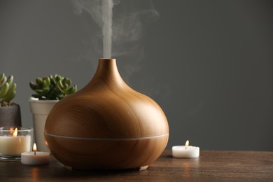 Aroma oil diffuser, houseplants and burning candles on wooden table, space for text