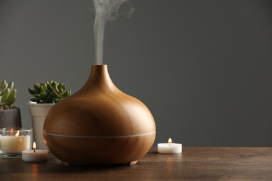 Photo of Aroma oil diffuser, houseplants and burning candles on wooden table, space for text