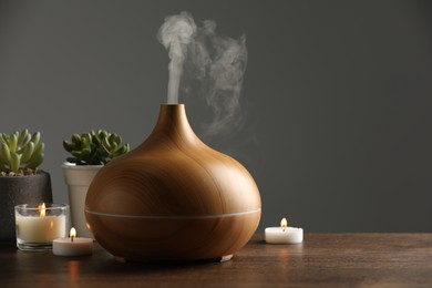 Photo of Aroma oil diffuser, houseplants and burning candles on wooden table, space for text