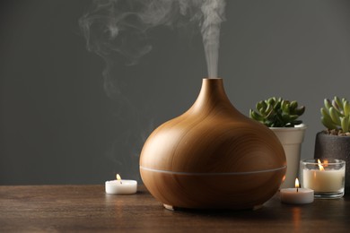 Aroma oil diffuser, houseplants and burning candles on wooden table, space for text