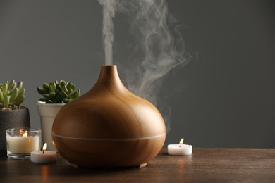 Aroma oil diffuser, houseplants and burning candles on wooden table, space for text