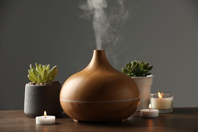 Photo of Aroma oil diffuser, houseplants and burning candles on wooden table