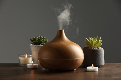 Photo of Aroma oil diffuser, houseplants and burning candles on wooden table