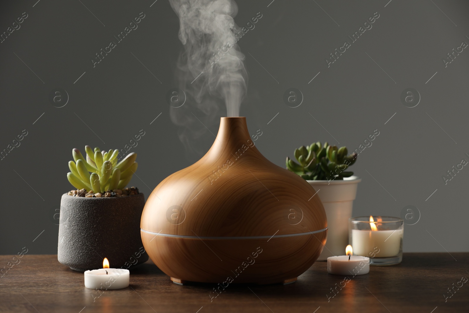 Photo of Aroma oil diffuser, houseplants and burning candles on wooden table