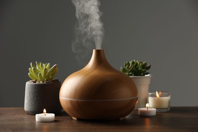 Photo of Aroma oil diffuser, houseplants and burning candles on wooden table