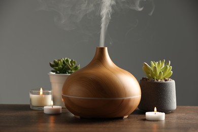 Photo of Aroma oil diffuser, houseplants and burning candles on wooden table