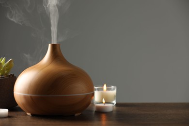 Aroma oil diffuser, plant and burning candles on wooden table, space for text