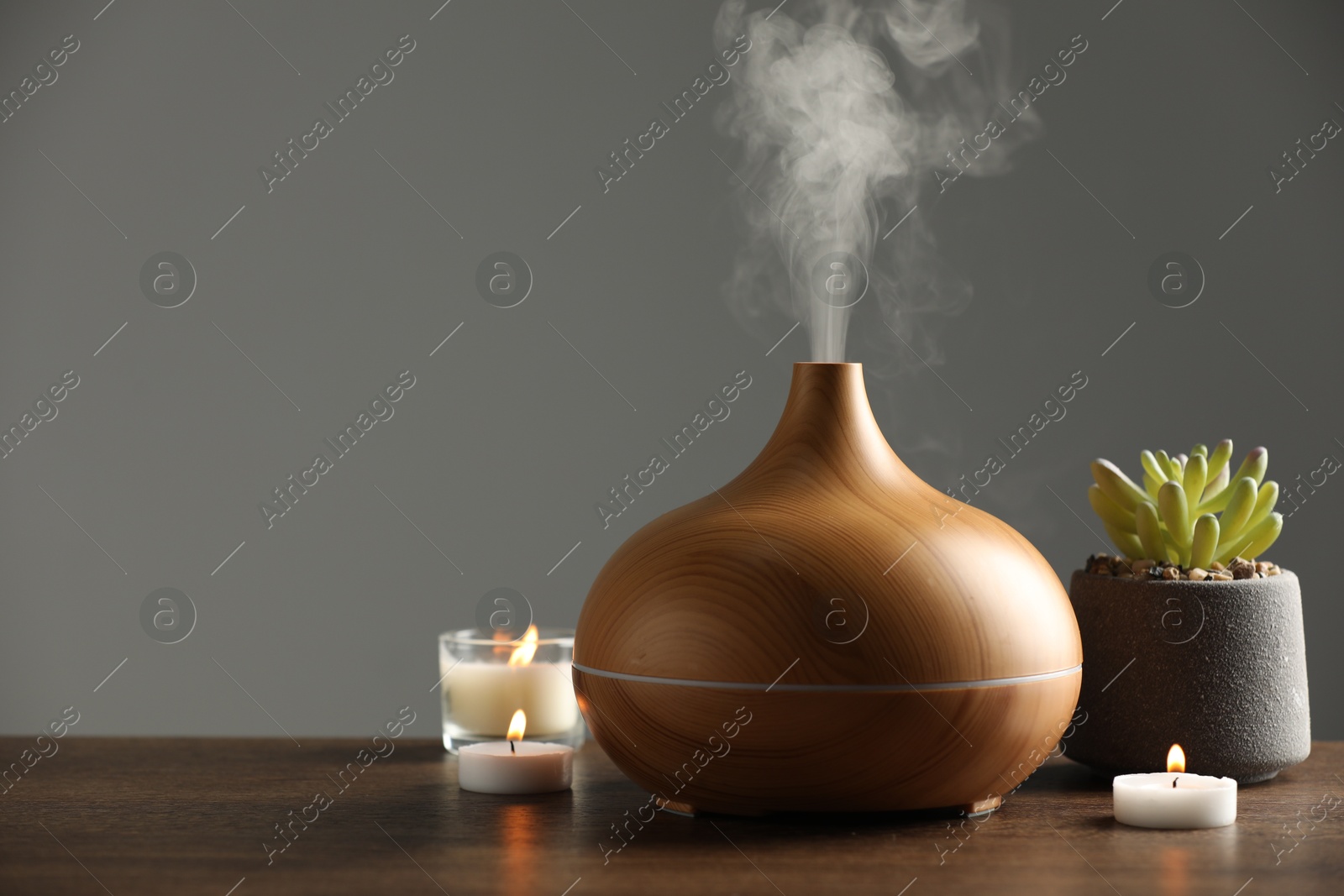 Photo of Aroma oil diffuser, plant and burning candles on wooden table, space for text