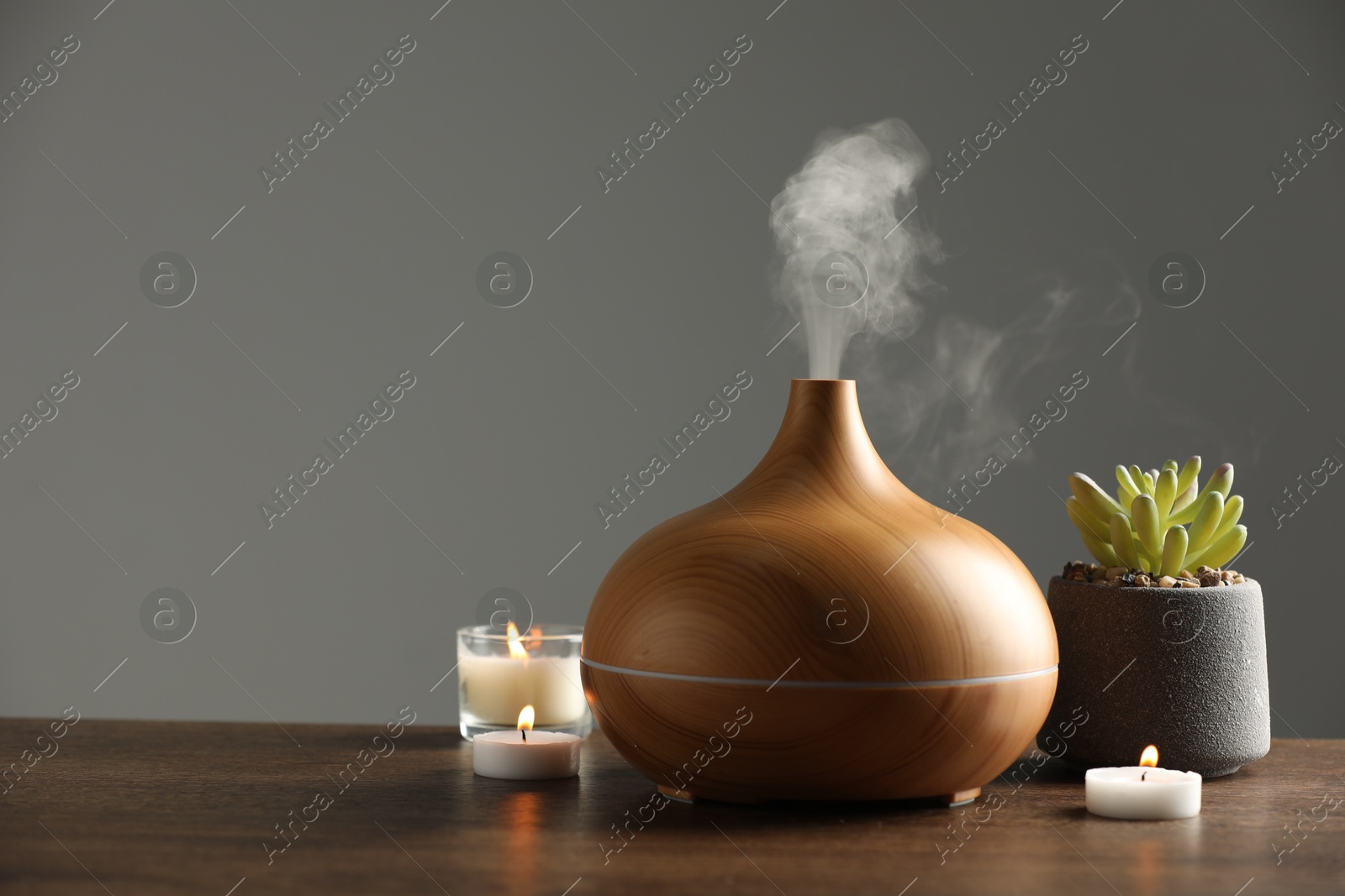 Photo of Aroma oil diffuser, plant and burning candles on wooden table, space for text