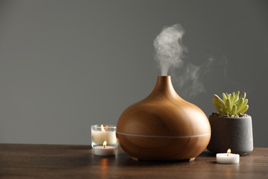 Aroma oil diffuser, plant and burning candles on wooden table, space for text