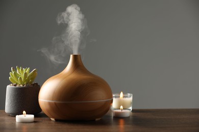 Aroma oil diffuser, plant and burning candles on wooden table, space for text