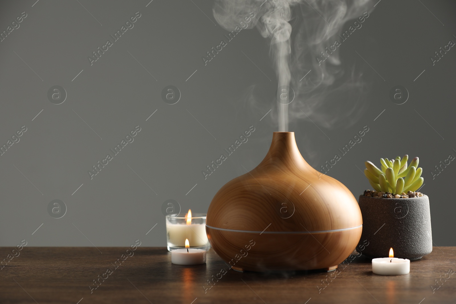 Photo of Aroma oil diffuser, plant and burning candles on wooden table, space for text