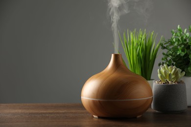 Photo of Aroma oil diffuser and houseplants on wooden table, space for text