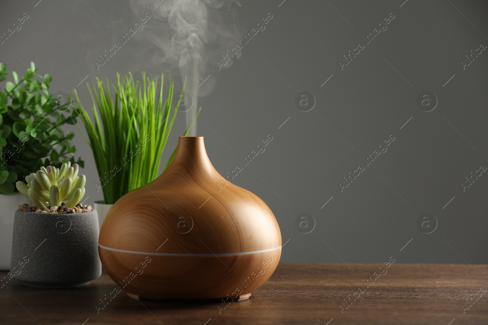 Photo of Aroma oil diffuser and houseplants on wooden table, space for text