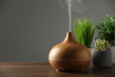 Aroma oil diffuser and houseplants on wooden table, space for text