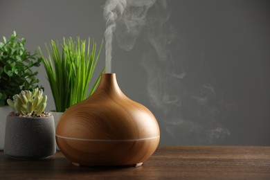 Photo of Aroma oil diffuser and houseplants on wooden table, space for text