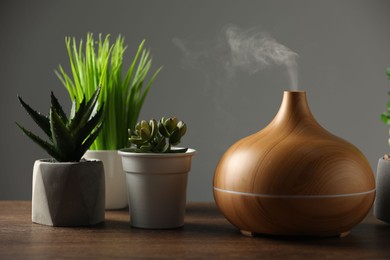 Aroma oil diffuser and houseplants on wooden table