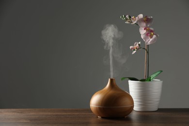 Aroma oil diffuser and orchid flower on wooden table, space for text