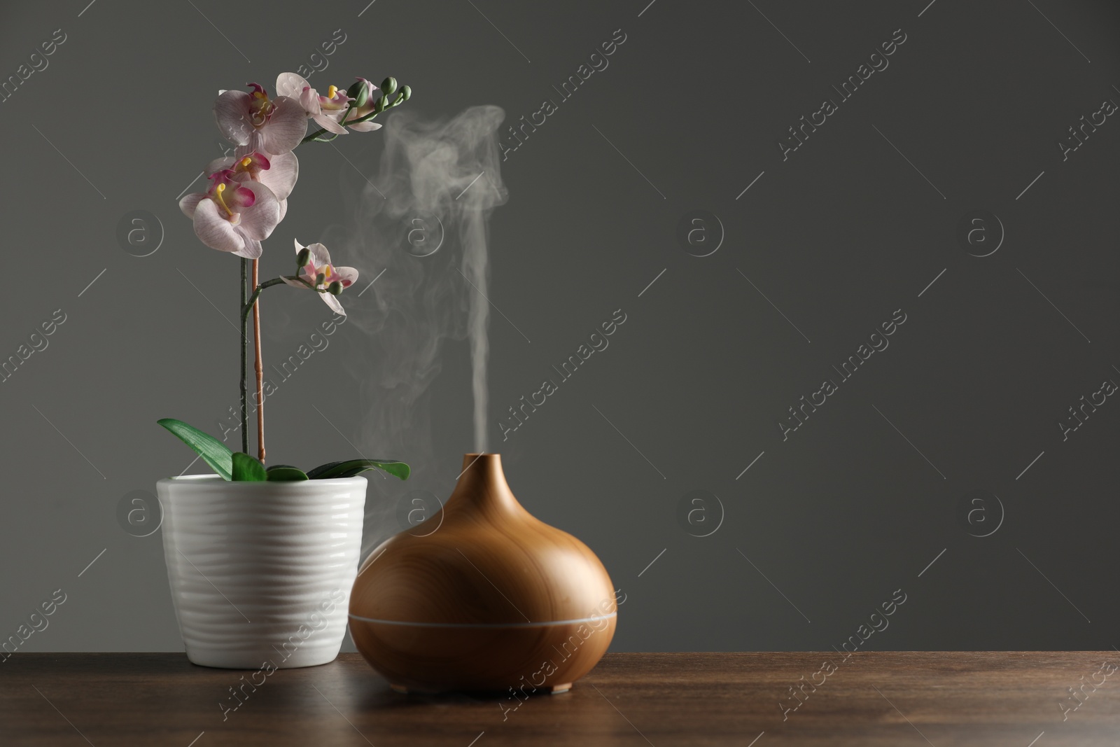 Photo of Aroma oil diffuser and orchid flower on wooden table, space for text